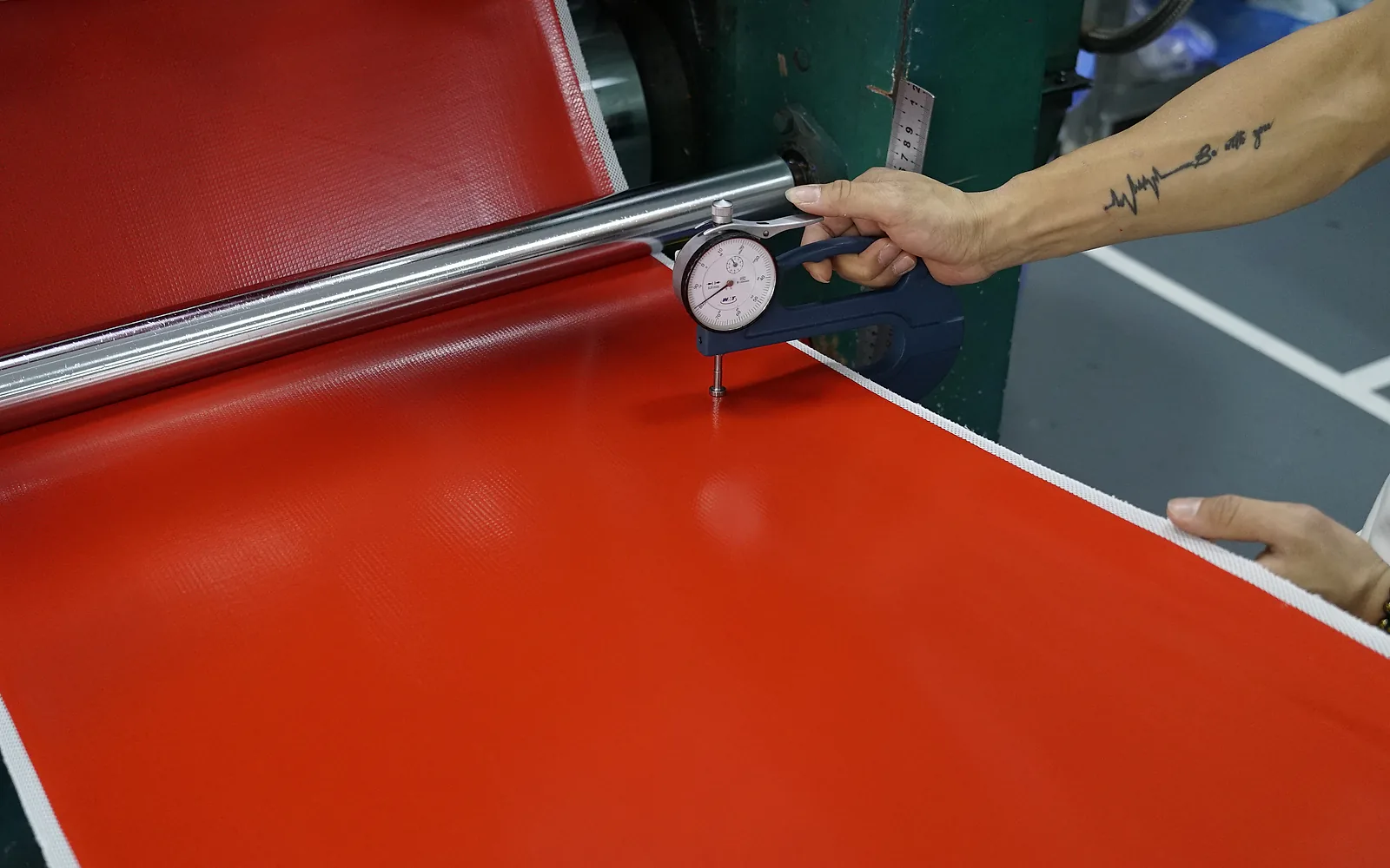 Operator checking coated reinforcement sheet thickness with a dial gauge